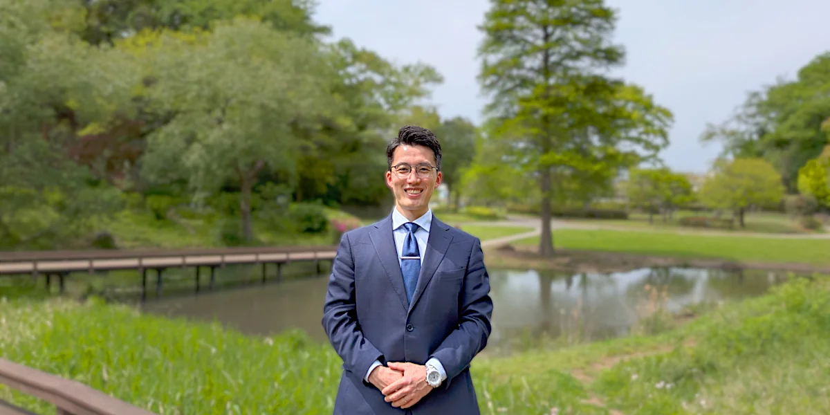 藤沢市の新林公園を背景に穏やかな笑顔で立つスーツ姿の代表・相田暁文